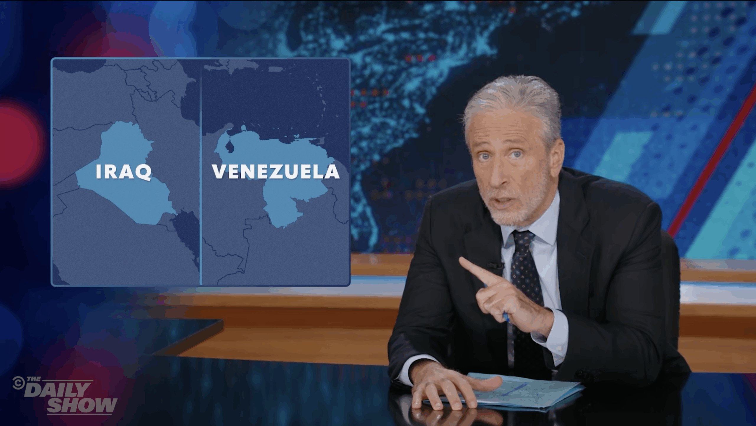 Jon Stewart on The Daily Show pointing to a graphic comparing maps of Iraq and Venezuela during a political commentary segment.